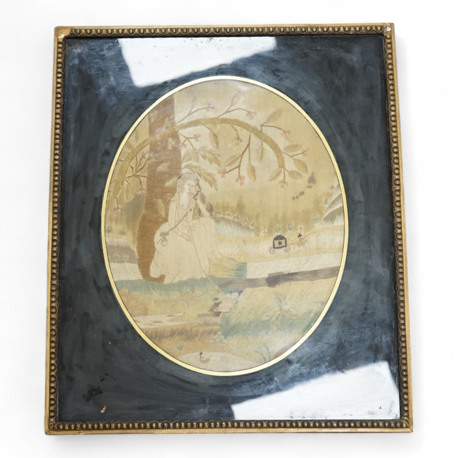 An early 19th century framed oval silk embroidery of a woman with a dog, overall 48cm high